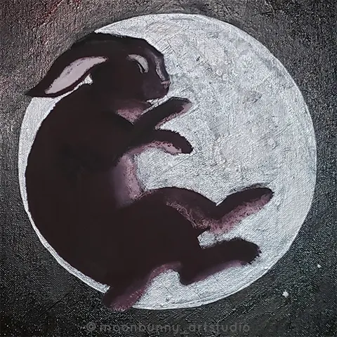 A black bunny resting on its side sleeping. It is laying on a full silver moon